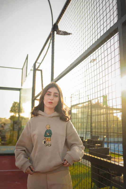 Beige oversized ELUX hoodie with minimal character graphic design worn outdoors in streetwear setting
